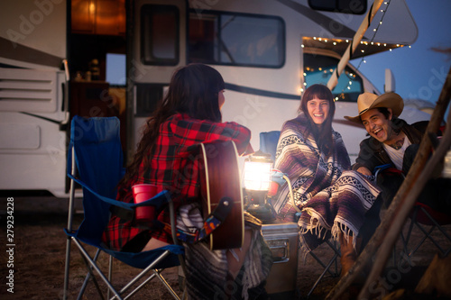 Εκτύπωση καμβά Smiling friends sitting by motorhome at dusk
