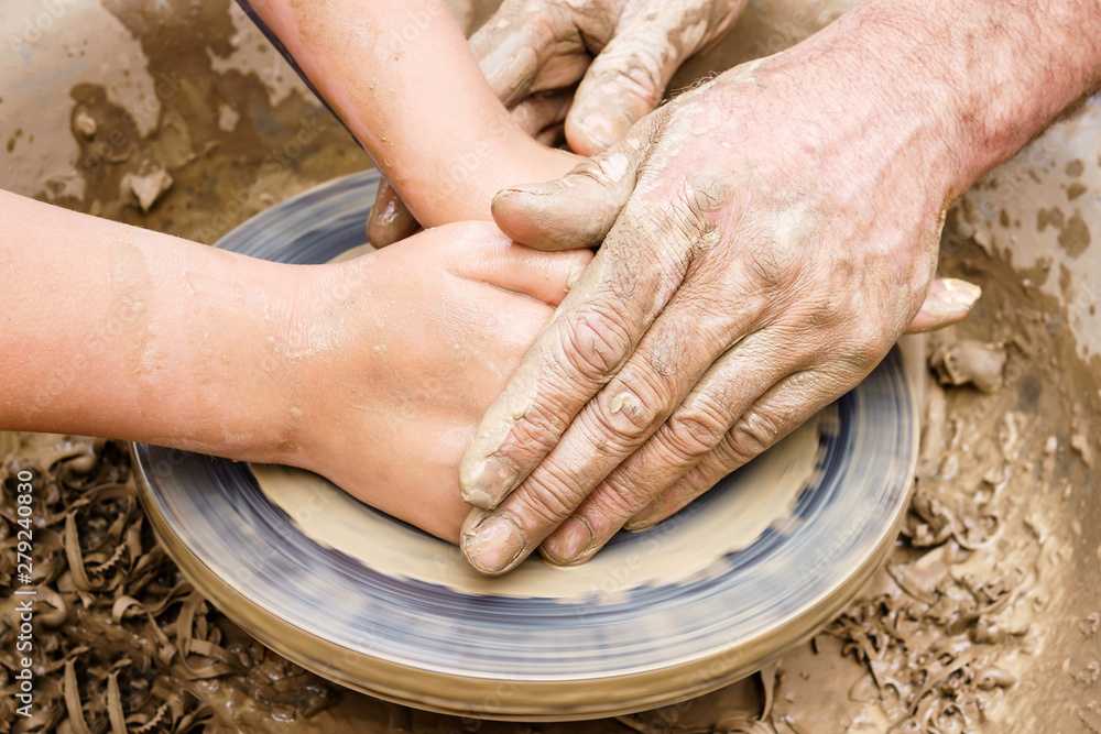 two pairs of hands create a clay product on a potter's wheel
