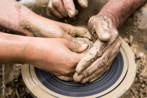 two pairs of hands create a clay product on a potter's wheel