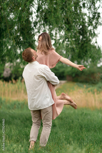 Young loving couple hugging and dancing on the green grass on the lawn. Beautiful and happy woman and man gently touch each other. Beautiful couple in love. girl in the dress and the guy in the shirt