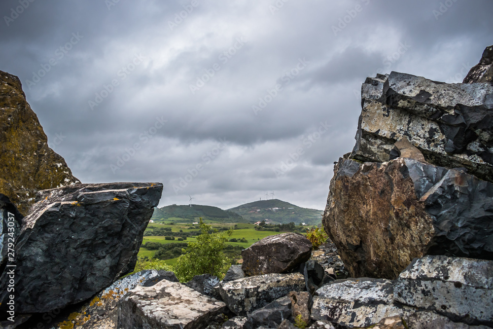 Green landscape with mountains and wind towers in background framed by rocks Green landscape with mountains and wind towers in background framed by rocks