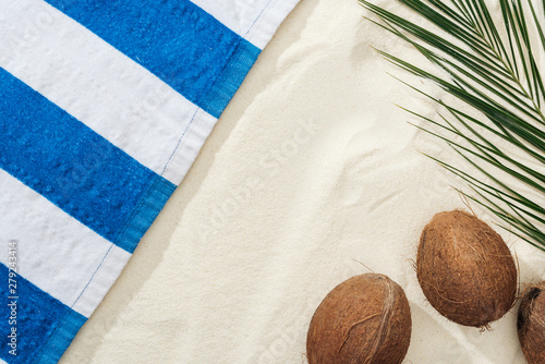 Photos top view of palm leaf, coconuts and striped towel on sand