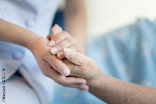 Nurse sitting on a hospital bed next to an older woman helping hands, care for the elderly concept