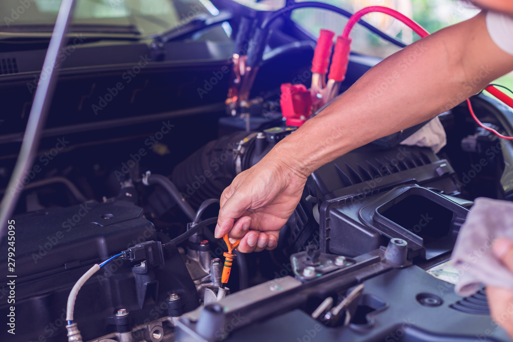 Mechanic repairing car with open hood,Side view of mechanic checking level motor oil in a car with open hood. blurry voltmeter for check voltage in battery. Repair service. Selective focus. Mechanic repairing car with open hood,Side view of mechanic checking level motor oil in a car with open hood. blurry voltmeter for check voltage in battery. Repair service. Selective focus.