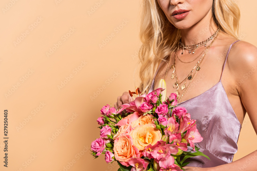 cropped view of elegant woman in violet satin dress holding bouquet of flowers isolated on beige with copy space