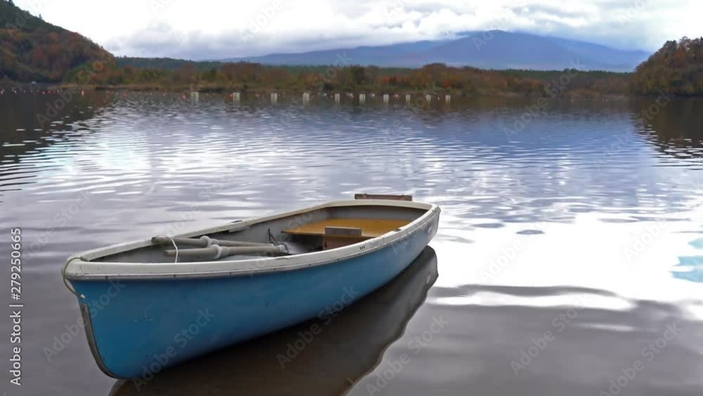 A small blue and white rowboat sits moored in the sandy bottom of a quiet lake surrounded by tall mountains and fall colored trees A small blue and white rowboat sits moored in the sandy bottom of a quiet lake surrounded by tall mountains and fall colored trees