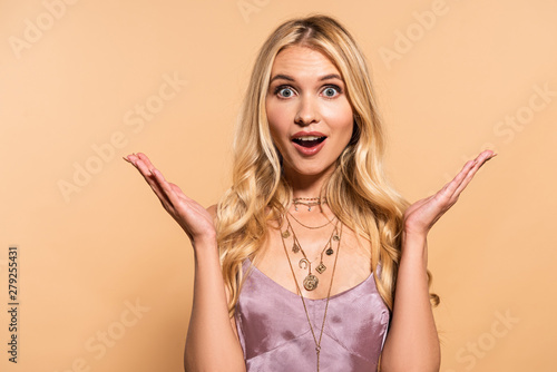 excited blonde woman in violet satin dress and necklace isolated on beige