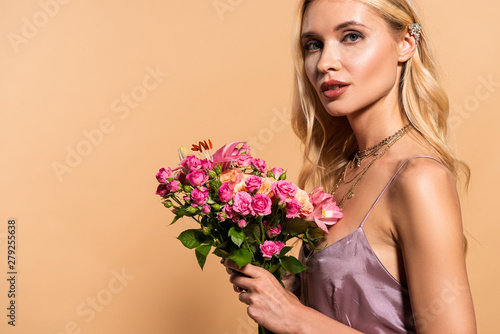 blonde woman in violet satin dress and necklace holding bouquet of flowers on beige