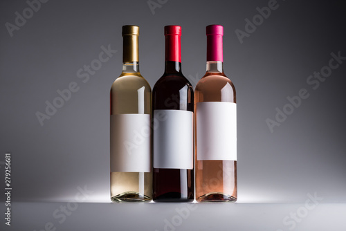 bottles of red, white and rose wine with blank labels on dark background with back light