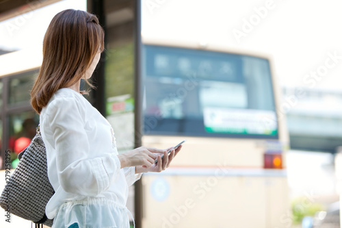 バス停でスマートフォンを操作する女性