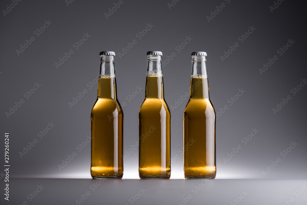 three glass bottles with beer in row on grey background three glass bottles with beer in row on grey background