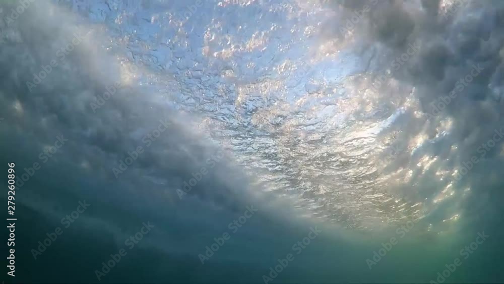 Slow motion underwater footage of boat hull passing very close with sunlight shining through water.