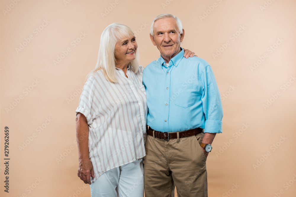 cheerful retired wife looking at husband standing with hand in pocket isolated on beige cheerful retired wife looking at husband standing with hand in pocket isolated on beige
