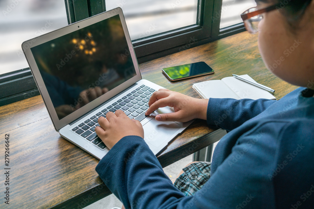 Asian student using laptop at cafeteria next to window