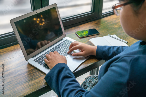 Foto Asian student using laptop at cafeteria next to window