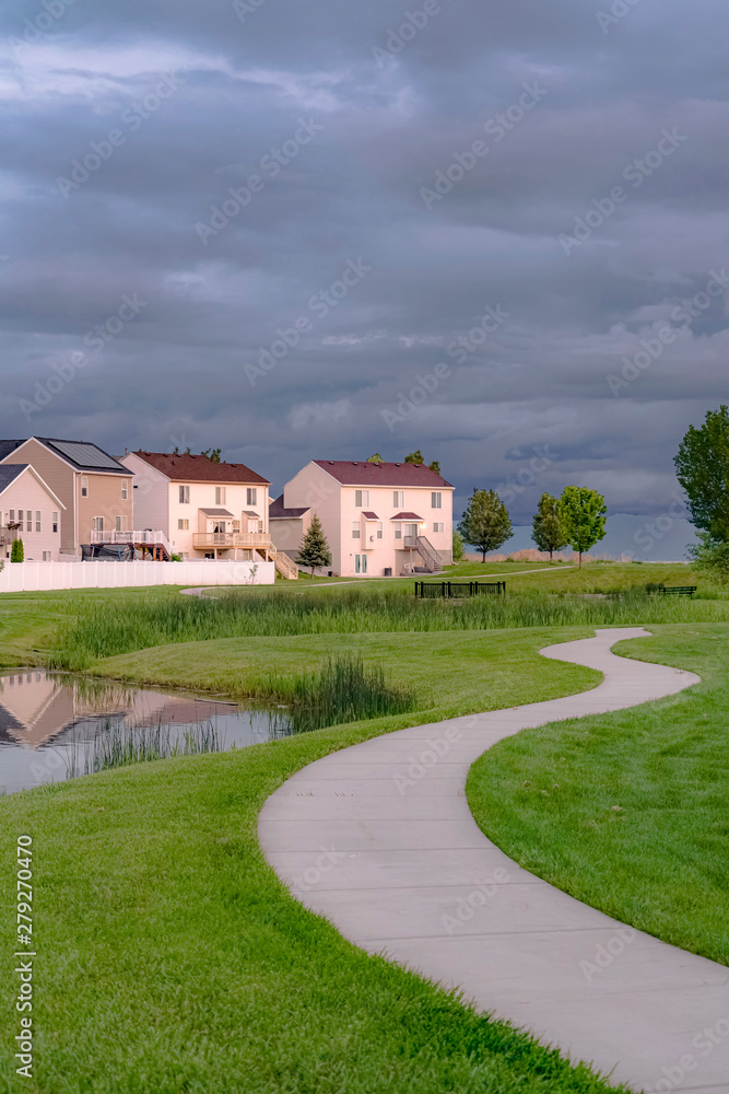 Neighborhood park with pond bridge and pathway under sky with thick gray clouds