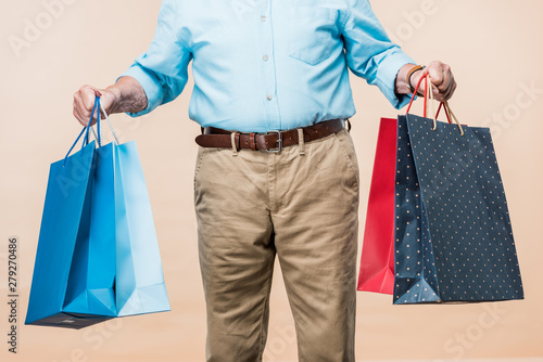cropped view of retired man smiling holding shopping bags isolated on beige