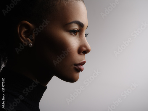 Closeup fashionable portrait of a metis young woman with perfect smooth glowing skin, full lips, collected hair and long neck. Studio photo of an african american female model face, profile