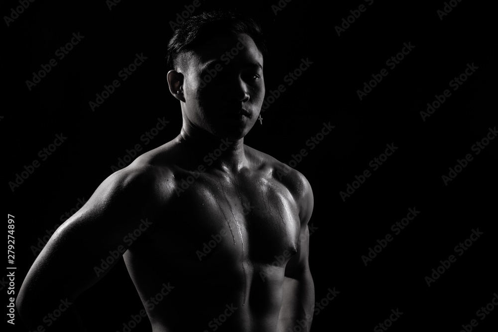 Naklejka premium Asian Big Muscle Fitness Man exercise show arms, bicep, chest with sweat from heat. Young Sport Male six packs shoot in low key lighting exposure with shadow contrast, copy space