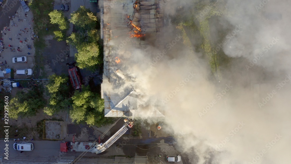 Obraz premium The roof of a residential house is burning. firefighters with a ladder extinguish a fire on the roof of a residential high-rise building
