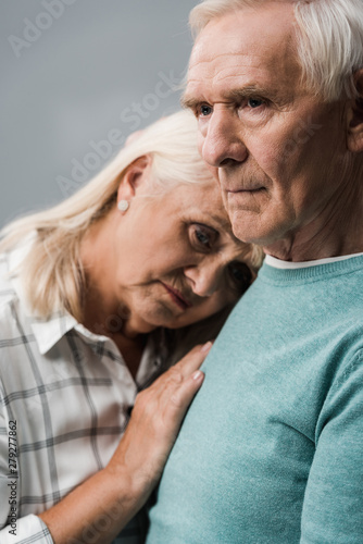 sad retired man near frustrated senior wife looking at camera isolated on grey