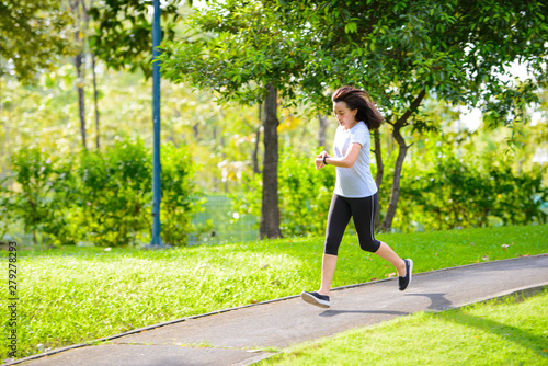 Young asian woman running in a city park and looks at the smart watch © brostock