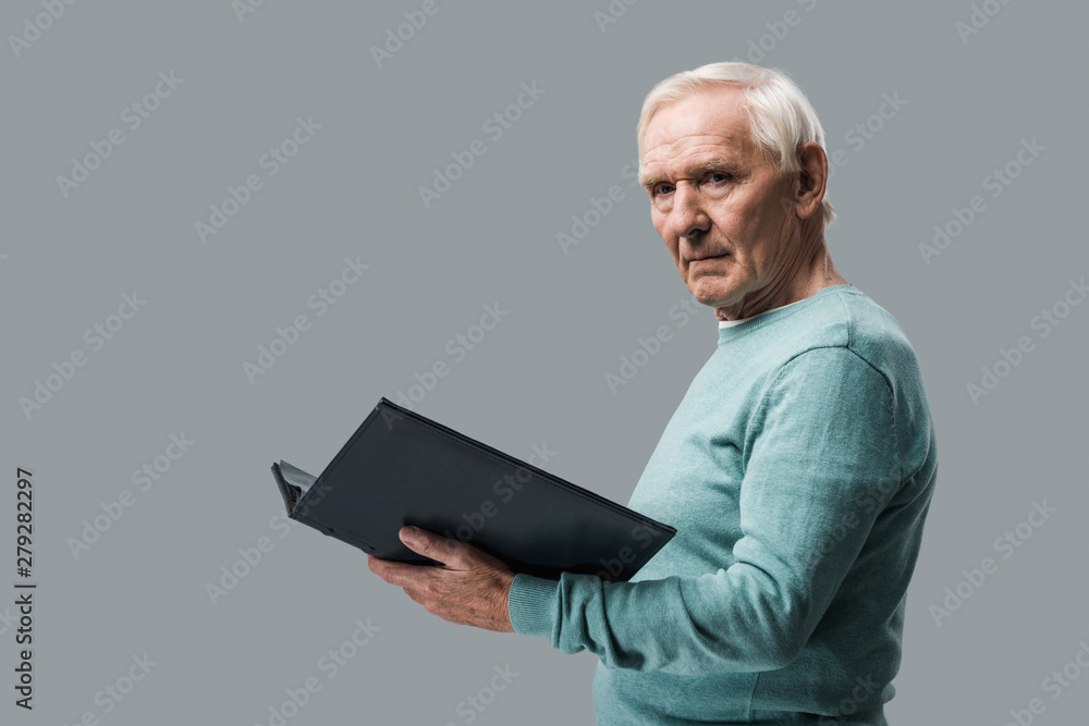 upset retired man with grey hair holding photo album isolated on grey upset retired man with grey hair holding photo album isolated on grey