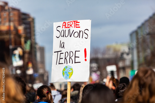 French sign held at ecological protest. A French sign is viewed close-up above the heads of environmental demonstrators, saying Alert, save the earth during a gathering in a city center. © Valmedia