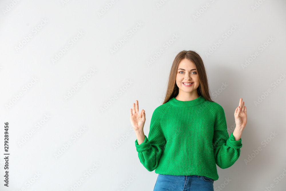 Young deaf mute woman using sign language on light background Young deaf mute woman using sign language on light background