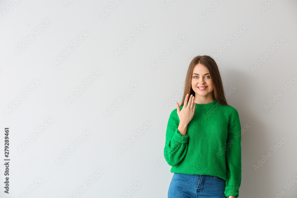 Young deaf mute woman using sign language on light background Young deaf mute woman using sign language on light background
