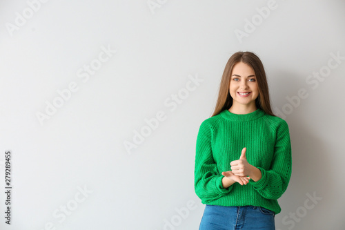 Young deaf mute woman using sign language on light background photo