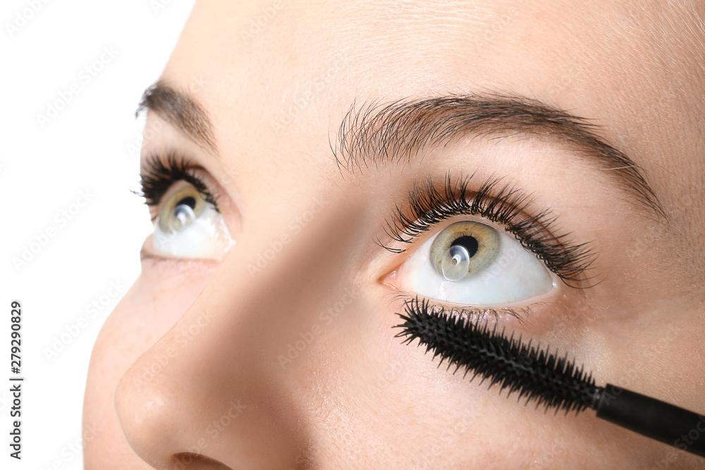 Naklejka premium Beautiful young woman with eyelash extensions applying mascara against white background, closeup