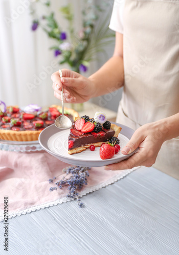 Woman eating tasty chocolate strawberry cake in kitchen