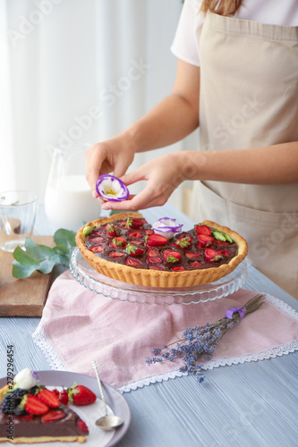 Woman decorating tasty chocolate strawberry cake with flower