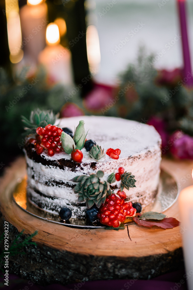 Delicate wedding white cake decorated with pomegranate and succulent surrounded by flowers and candles. Delicate wedding white cake decorated with pomegranate and succulent surrounded by flowers and candles.