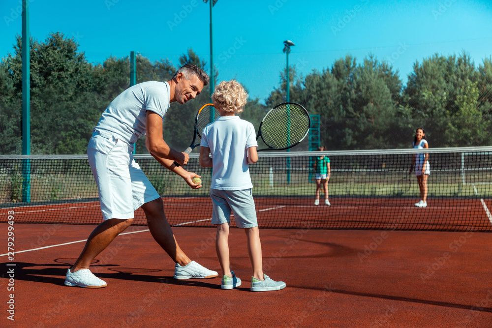 Father teaching his cute curly son to play tennis with family