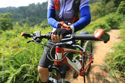 Cross country biking woman cyclist set the smartwatch while riding bike in forest on sunny day