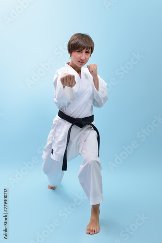 Young karate woman in a white kimono with black belt demonstrates fighting stances and strikes. Girl at studio shows martial arts
