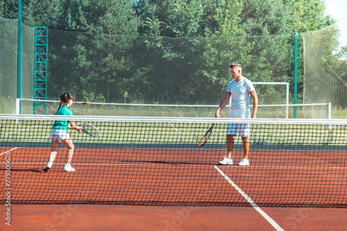 Dark-haired girl running while playing tennis with daddy