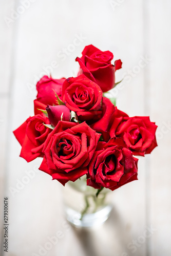 Close up of red rose bouquet in the vase on white wooden background