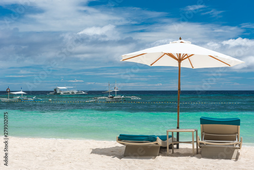 Tropical beach background from Alona Beach at Panglao Bohol island with Beach chairs on the white sand beach with cloudy blue sky and palm trees. Travel Vacation photo