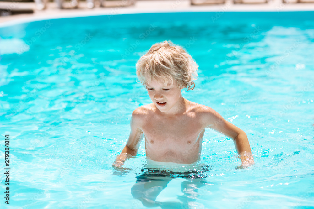 Curly boy enjoying sun and swimming in pool