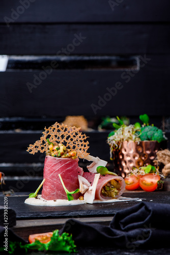 Beautiful serving of slice salted tuna with vegetables in a creamy sauce on a dark plate on a rustic wooden tray