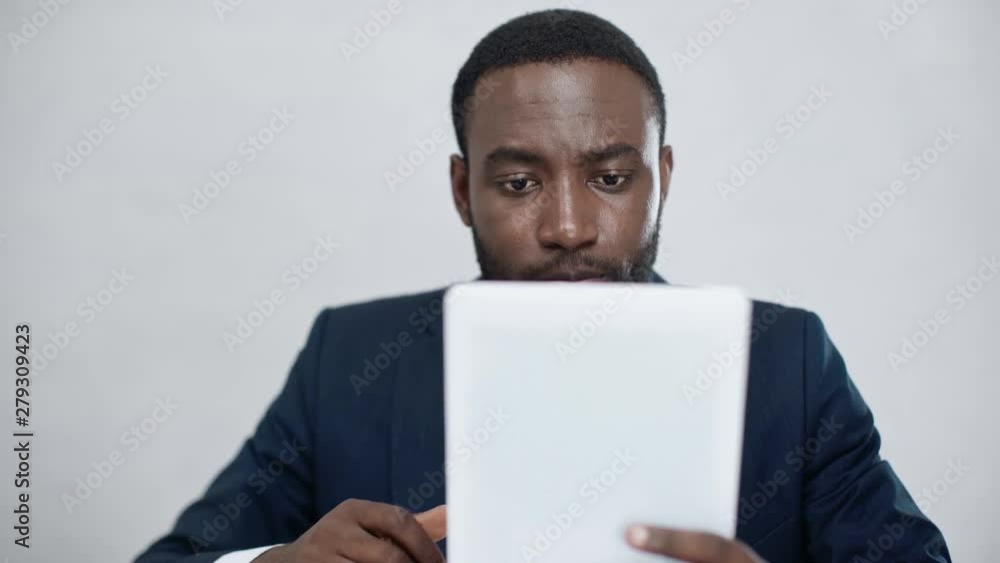 attentive african american businessman using digital tablet while drinking coffee in office attentive african american businessman using digital tablet while drinking coffee in office