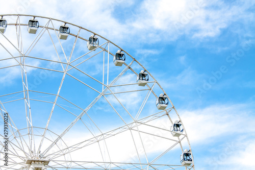 View of a part of a white ferris wheel against a blue sky with snow-white clouds in an amusement park.