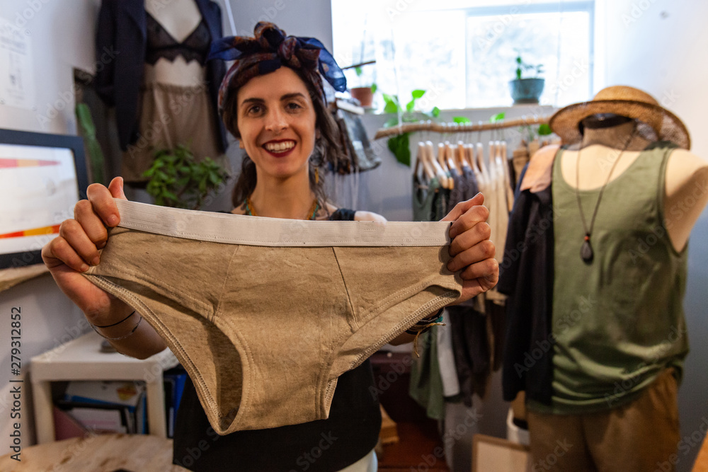 Fashion designer is showing underwear. A young caucasian dressmaker looks happy as she shows eco-friendly beige colored underwear created by hand in design studio. Fashion designer is showing underwear. A young caucasian dressmaker looks happy as she shows eco-friendly beige colored underwear created by hand in design studio.
