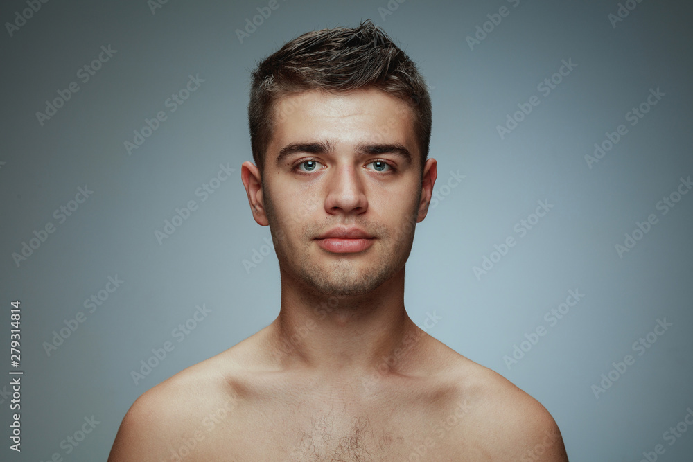 Portrait of shirtless young man isolated on grey studio background. Caucasian healthy male model looking at camera and posing. Concept of men's health and beauty, self-care, body and skin care. Portrait of shirtless young man isolated on grey studio background. Caucasian healthy male model looking at camera and posing. Concept of men's health and beauty, self-care, body and skin care.