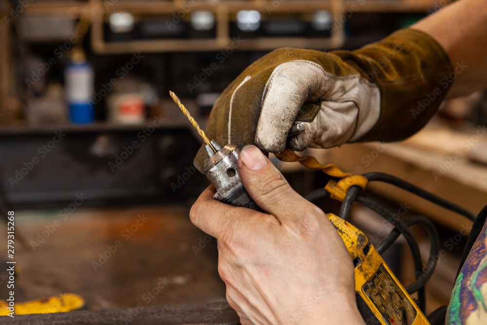 Obraz premium Blacksmith changing a drill bit. A closeup view on the dirty hands of a metalworker using the chuck of a power drill to replace a spotting bit, used for marking and drilling holes in steel.
