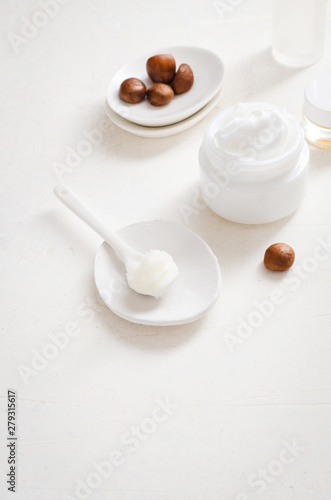 Shea butter in ceramic spoon on white background with nuts and moisturizer creme. Free text space.