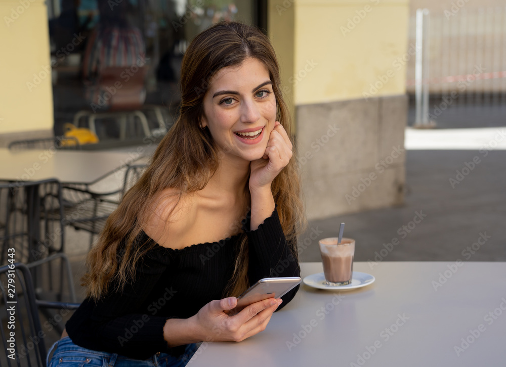 Attractive young woman chatting and dating on smart mobile phone in coffee shop outside city street Attractive young woman chatting and dating on smart mobile phone in coffee shop outside city street